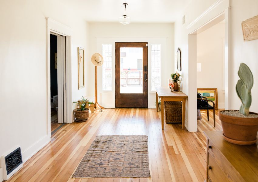 An entrance to a home is pictured with natural lighting, light wooden floors and white walls.